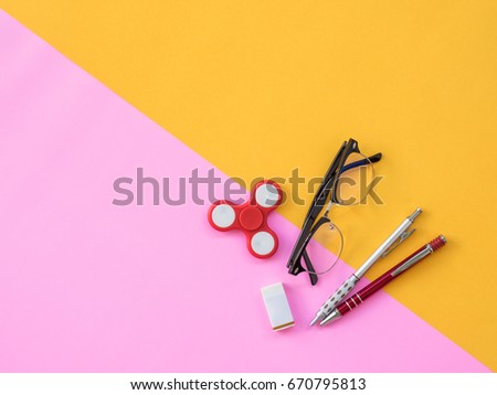 Stationary Background. Flat Lay Photo of Stationary with hand spinner, glasses and stationary on pink and yellow background