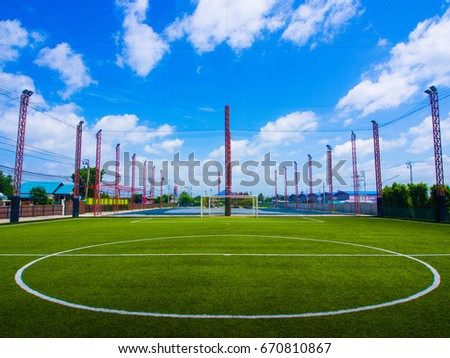 Beautiful view of a green soccer turf field with the light poles in red color and blue sky with clouds. A field for recreation.