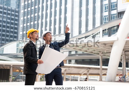 Male employees wear yellow helmet, holding a pose drawings. Hand pointing to construction. The progress of construction. Shows confidence and conviction. negotiation Successful and complete deal conce Royalty-Free Stock Photo #670815121