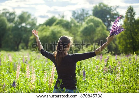 Young girl with bunch of flowers having fun and feeling freedom on the lupines flower field.Summer day, back view, horizontal picture