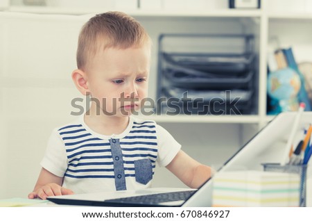 Young cute kid is watching cartoons on laptop in the office.