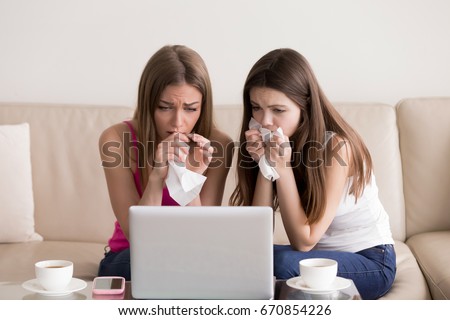 Two sentimental women friends upset crying and wiping tears with handkerchiefs while watching dramatic, sad movie, TV reality show or touching old home video on laptop while sitting on sofa at home  Royalty-Free Stock Photo #670854226