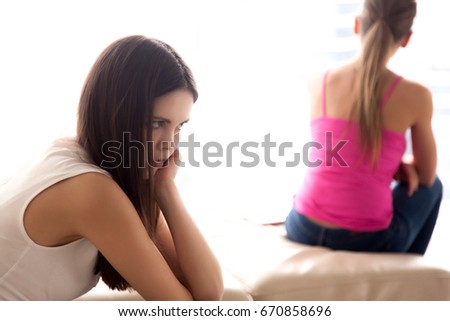 Upset teen girl worries because of conflict with girlfriend, annoyed, sorry , feeling guilty after mutual insults, harsh words. Two young offended ladies sit separately not talking to each other  Royalty-Free Stock Photo #670858696