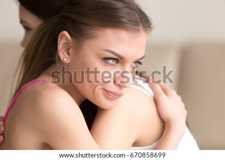 Young woman with dissatisfied and angry facial expression embracing girlfriend, insincere female hiding her envy or jealous, thinking about deception. Distrust between close relatives or old friends Royalty-Free Stock Photo #670858699