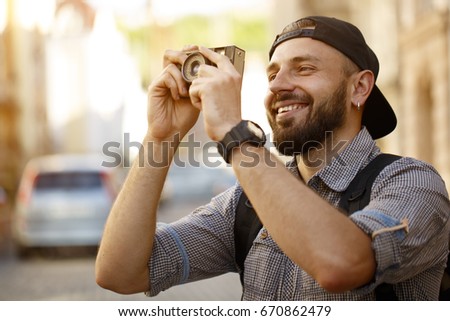 Handsome bearded man smiling happily taking pictures with his vintage instant camera enjoying sightseeing in a beautiful city copyspace emotions travelling tourism vacation memories travel lifestyle
