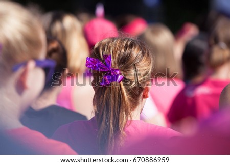 Hair pony tail with pink ribbon as a symbol for fighting cancer. Surrounded by ladies wearing pink all raising money to fight cancer. With a vignette. Royalty-Free Stock Photo #670886959