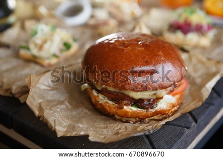 Big tasty burger with ham cutlet meat & fresh vegetables served on decorative brown paper in restaurant.Hamburger dish in cafe.