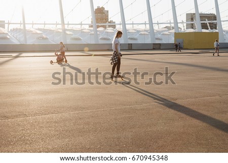 Hipster girl riding skate board in the city at sunset