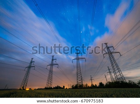Silhouette of electricity pylons and high-voltage power lines on the wheat field at dusk. Four electricity pylons in a row on the background of beautiful sky. Electrical Power Grid at twilight.