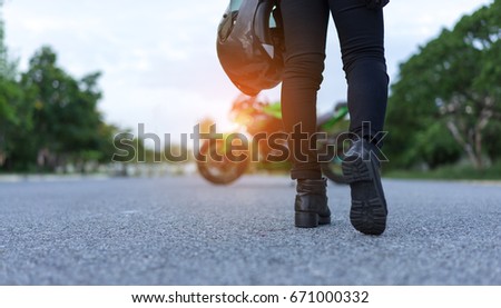Young woman biker holding helmet equipment with jacket for safety protection when over high speed walking to motorcycle on street travel lifestyle.
