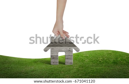 Hand pick a wooden house on green grass field area isolated on white background with clipping path.