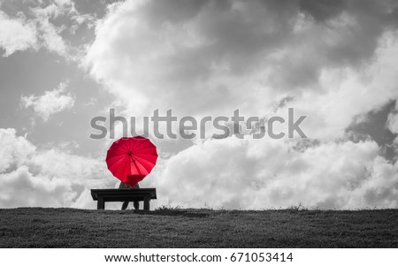 a women sitting alone on a bench with a red heart shaped umbrella waiting for love