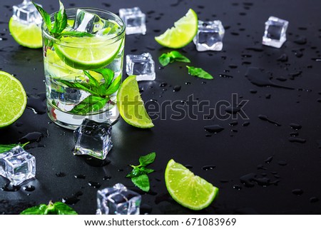Mojito cocktail with lime, ice cubes and mint in highball glass on a black background. Copy space