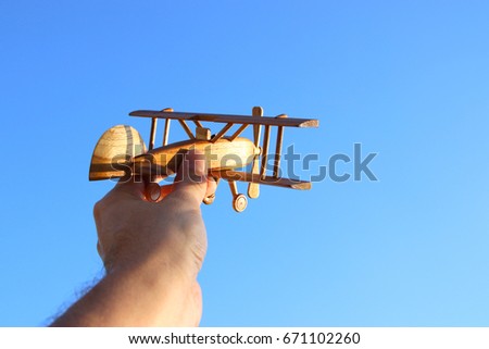 close up photo of man's hand holding wooden toy airplane against blue sky