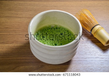 Matcha green tea in ceramic traditional chawan (tea bowl) with bamboo tea whisk on the wooden tray