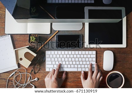 A male hand typing on a computer keyboard on a wooden desk.