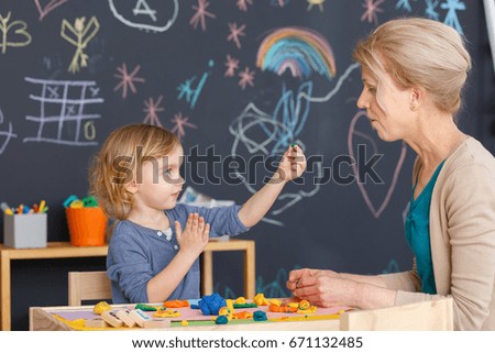Little girl and her teacher playing with plasticine during art classes