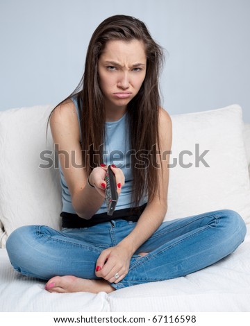 Attractive girl sitting on a sofa holding a remote control with a bored expression
