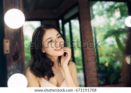 Pretty happy asian woman watching on herself in a big mirror at home.