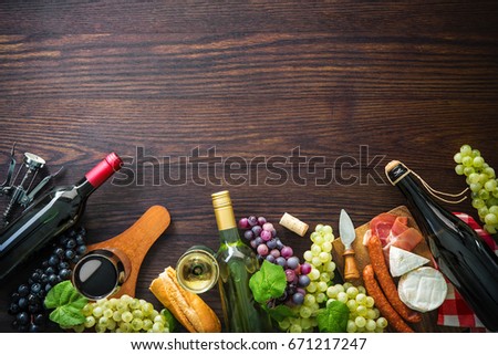 Wine bottles with grapes, cheese, ham and corks on wooden background with copy space