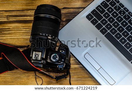 Modern DSLR camera and laptop on rustic wooden table. Top view