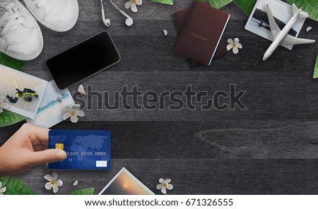 Top view of travel accessories. Hand holding Credit card, Passport, Seascape photos,Airplane, Smartphone , Sneakers and Plumeria flower on wooden background. Using credit card for travel and shopping.
