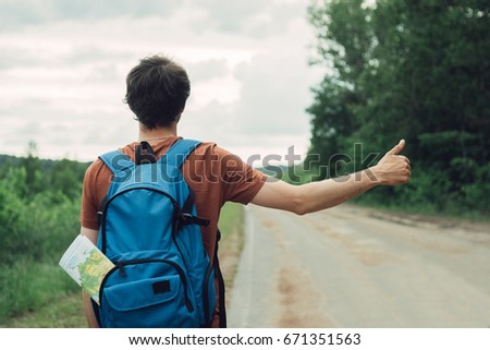 Young man traveller hitch hiking on empty road, closeup Royalty-Free Stock Photo #671351563