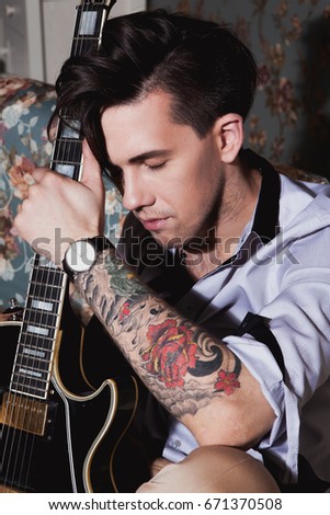 Musician with a tattoo of flowers on his arm holds a guitar