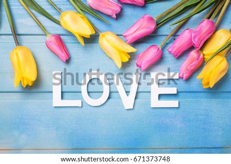Word love and  pink, yellow and white flowers on blue wooden background. Love concept. Selective focus. 