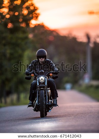 Man riding sportster motorcycle on countryside during sunset. Royalty-Free Stock Photo #671412043