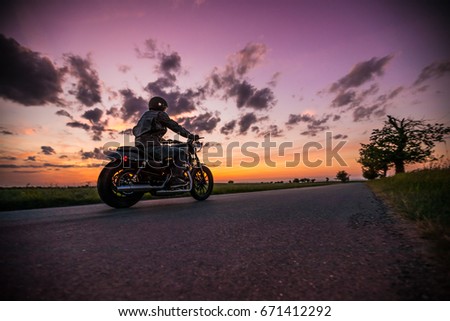 Man riding sportster motorcycle on countryside during sunset. Royalty-Free Stock Photo #671412292