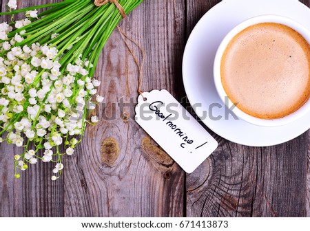 Cup of cappuccino and a bouquet of white lilies of the valley on a gray wooden background, top view