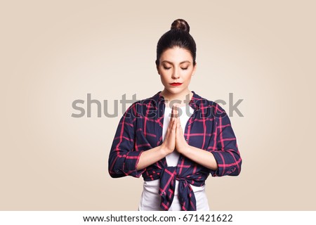 Young brunette woman practicing yoga, holding hands in namaste and keeping her eyes closed. Caucasian girl meditating indoors, praying for peace and love, having calm and peaceful facial expression.