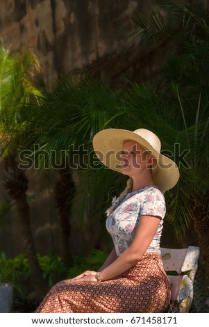 White girl with hat sitting on a chair at the entrance to the temple of the big Buddha. Thailand. Phuket