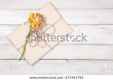 Paper wrapped package with dry rose on white wooden background