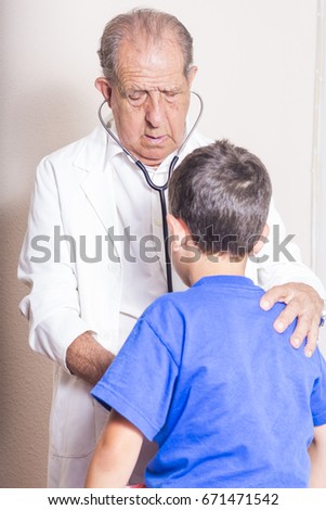 Senior male doctor with stethoscope examining a young boy child at hospital