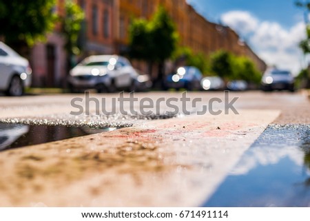 Sunny day after rain in the city, parked in the street car. Close up view from the puddle level near the dividing line on the asphalt