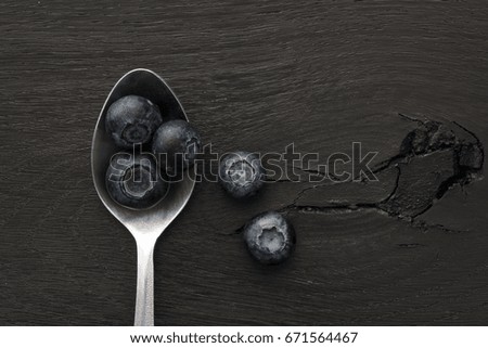 Spoonful of blueberries on black wooden background