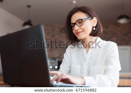 Adult elegant businesswoman in white shirt and glasses sitting with laptop in cafe.  Royalty-Free Stock Photo #671596882