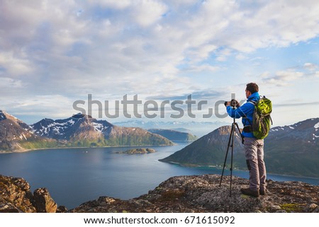 landscape photographer working with tripod and dslr camera in beautiful wild nature, standing with backpack on top of mountain