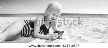 Sun kissed beauty. smiling blond girl in swimwear on the seashore viewing photos on camera