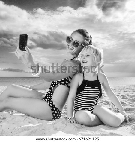 Sun kissed beauty. happy healthy mother and daughter in swimsuit on the seashore with digital camera taking selfie