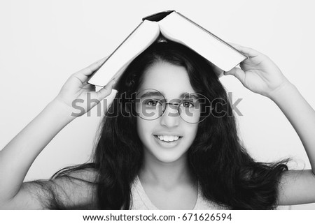 Adorable girl studying with eyeglasses and book on the head on white background