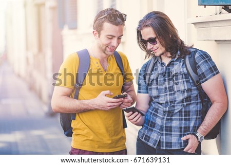 Two young men comparing phone models, using their smart phones, enjoying some funny internet content outdoors