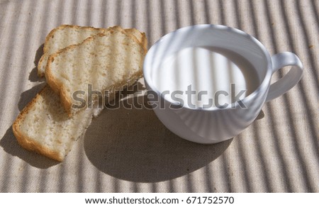 A glass of milk and pieces of white bread. The shadow of the blinds falls on the picture.