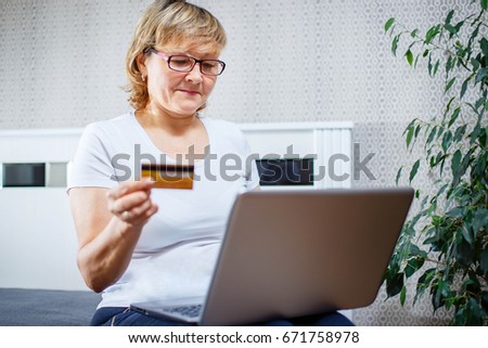 Old people and modern technology concept. Portrait of a 50s mature woman hand holding credit card, using online internet payment at home. Indoor senior people living lifestyle.