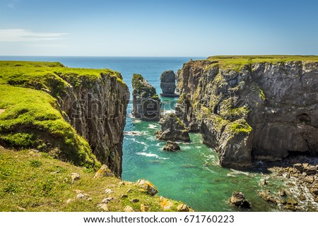 A view of rock stacks offshore from the top of a secluded cove along the Pembrokeshire coast, Wales in summer  Royalty-Free Stock Photo #671760223