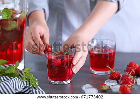 Woman decorating glass of strawberry lemonade in kitchen