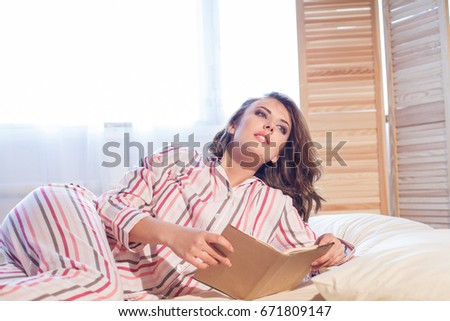 girl in pajamas lying on the bed and reading a book