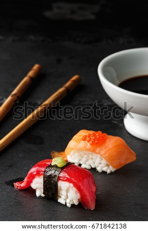  Red tuna Nigiri with Nori seaweed and wasabi paste on black slate stone with chopsticks and bowl of soy sauce. Raw fish in traditional Japanese sushi style. Vertical image. Royalty-Free Stock Photo #671842138